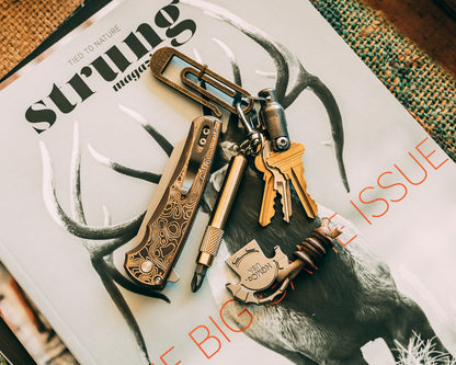 Brass screwdriver keychain and keys attached to JRW tough clip laying on top of a magazine next to a Pro-tech pocket knife.