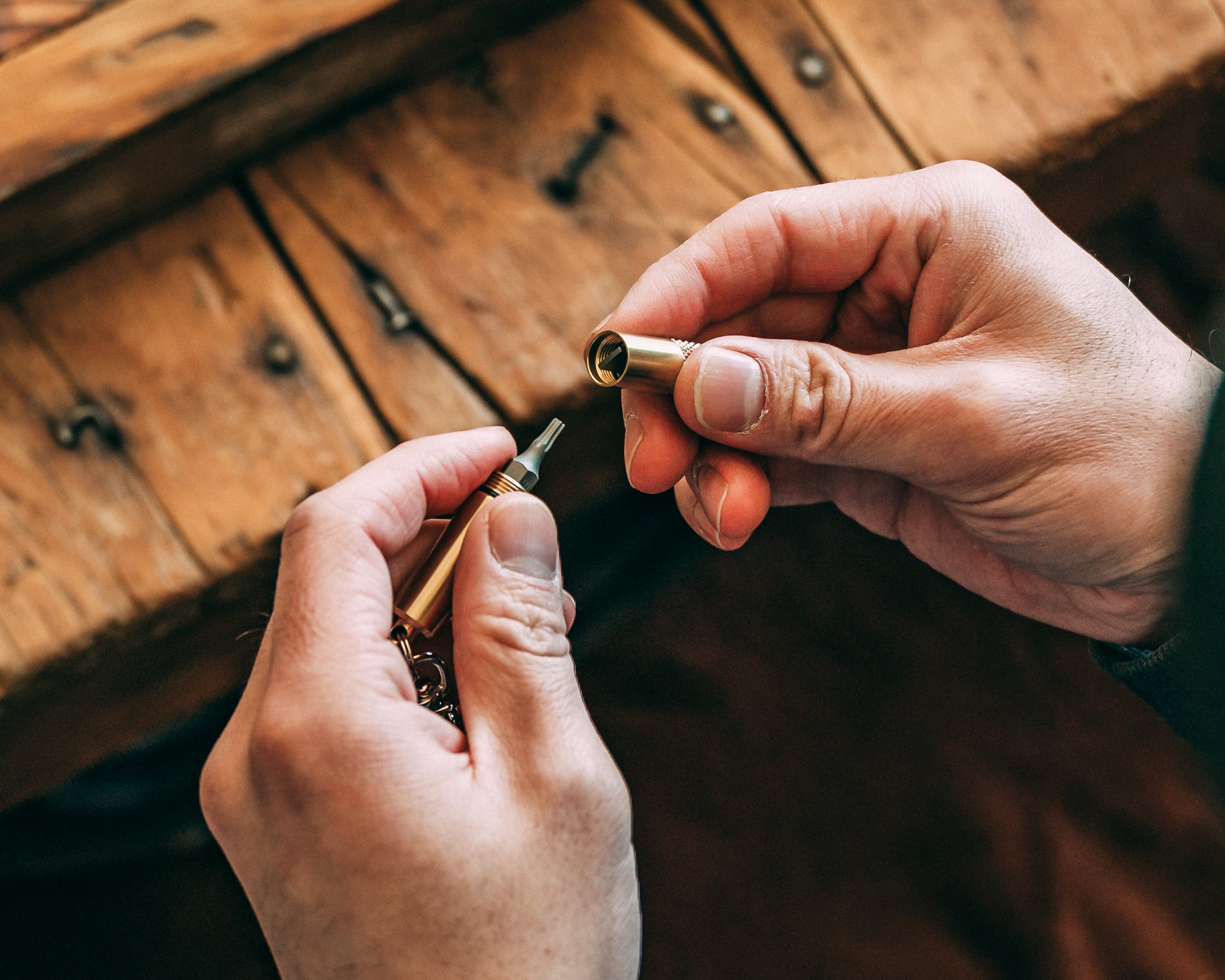 Pair of hands with brass screwdriver keychain opened up to reveal bit storage