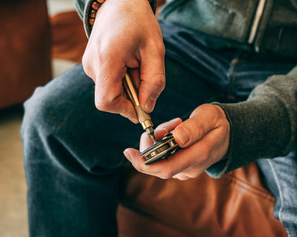 Pair of hands holding brass screwdriver keychain with bit being used to tighten pivot screw on utility tool.